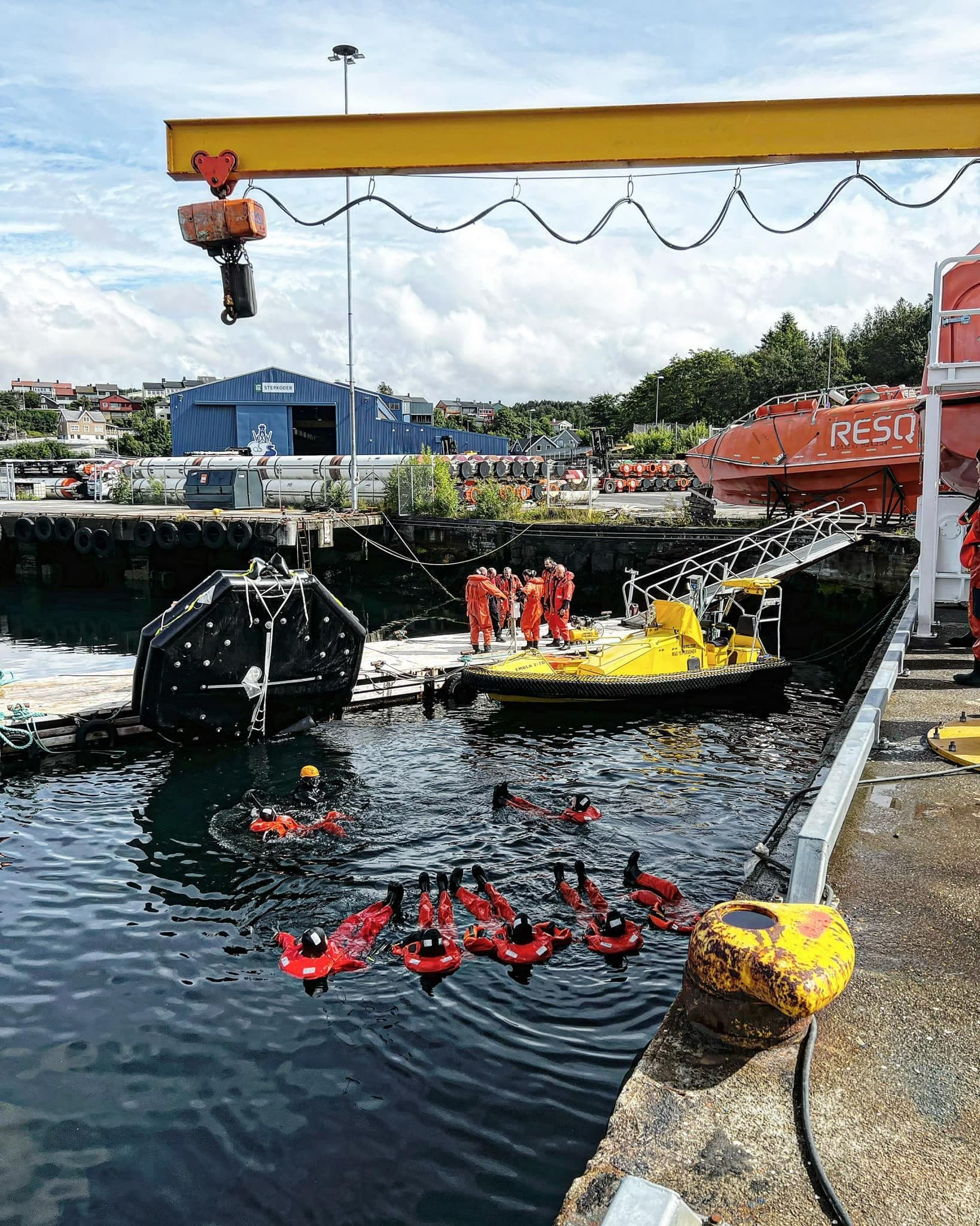 Trainees practising water survival techniques at a maritime training facility, guided by instructors, with a focus on safety and rescue skills in a controlled environment.